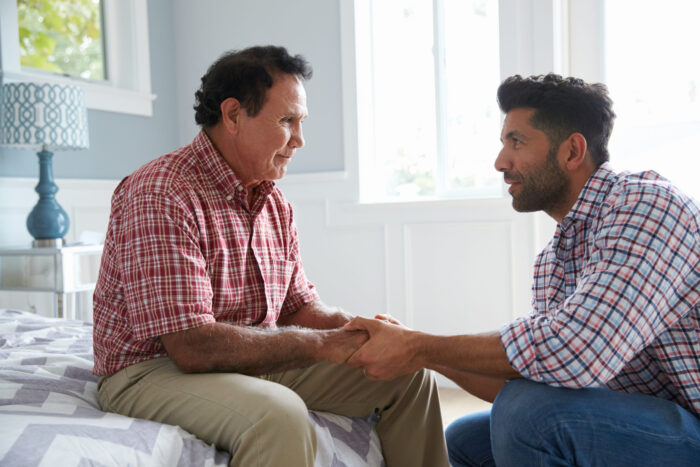 Son and father holding hands talking about senior living