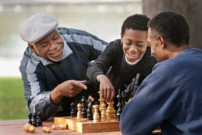 senior and grandson playing chess in the park