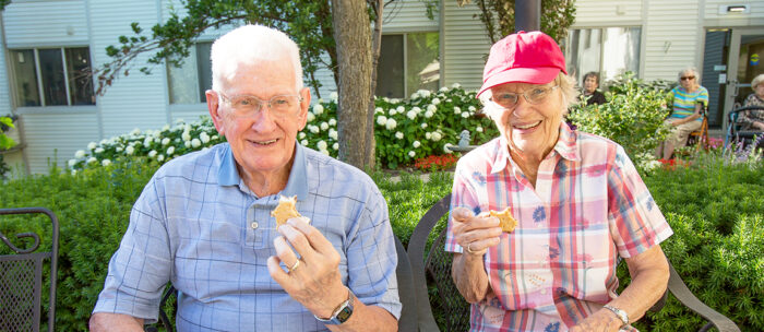 two senior living residents enjoying the summer weather and practicing summer safety tips on a bench while eating ice cream