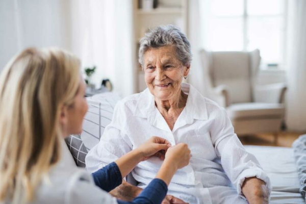 caregiver helping senior woman button shirt