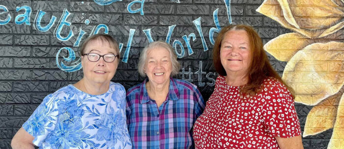three women standing in front of a mural