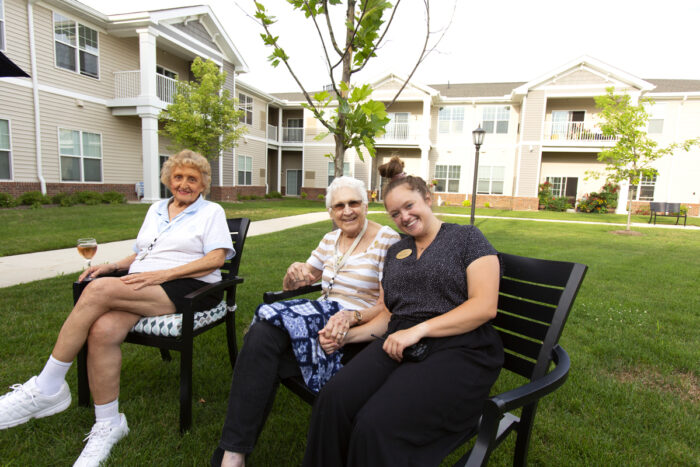 two residents and a caregiver sitting outside smiling