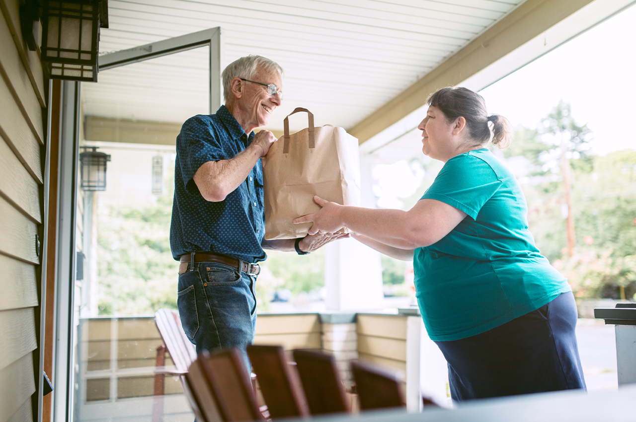 woman handing a senior a grocery bag